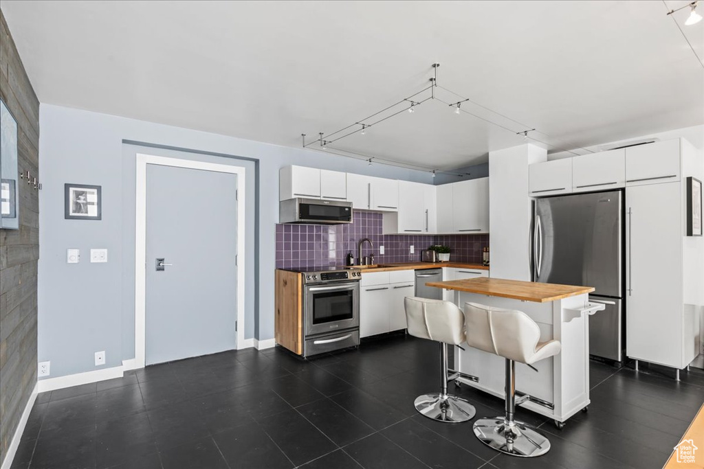 Kitchen with wooden counters, stainless steel appliances, white cabinets, sink, and a breakfast bar