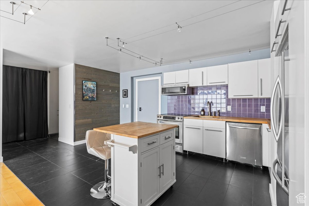 Kitchen featuring stainless steel appliances, a kitchen island, a kitchen bar, wood counters, and white cabinets