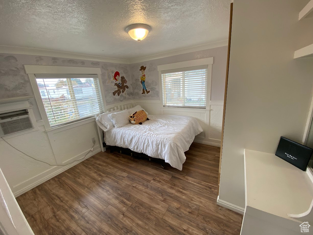 Bedroom with a textured ceiling, multiple windows, dark hardwood / wood-style floors, and ornamental molding