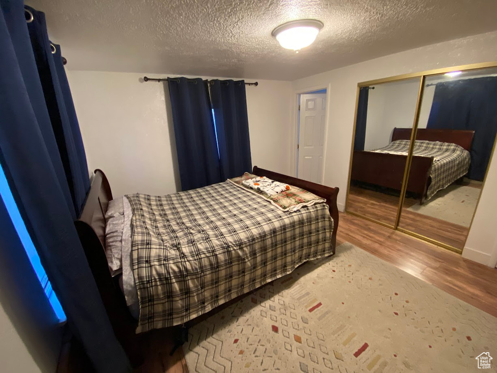 Bedroom with a textured ceiling, hardwood / wood-style flooring, and a closet