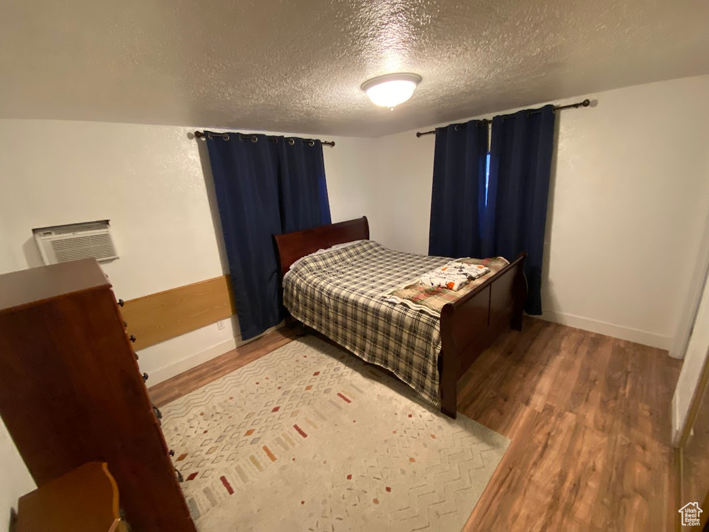 Bedroom with hardwood / wood-style floors, a wall mounted air conditioner, and a textured ceiling