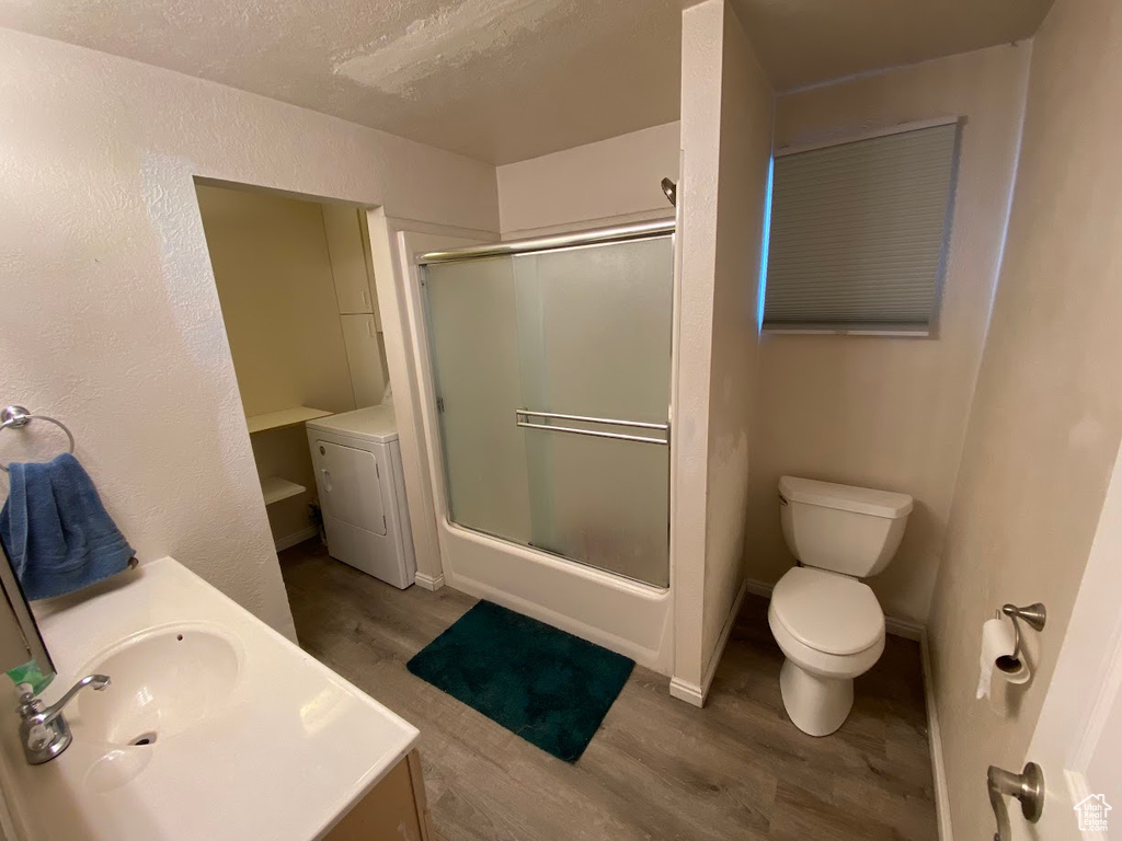 Full bathroom with vanity, hardwood / wood-style flooring, enclosed tub / shower combo, washer / dryer, and toilet