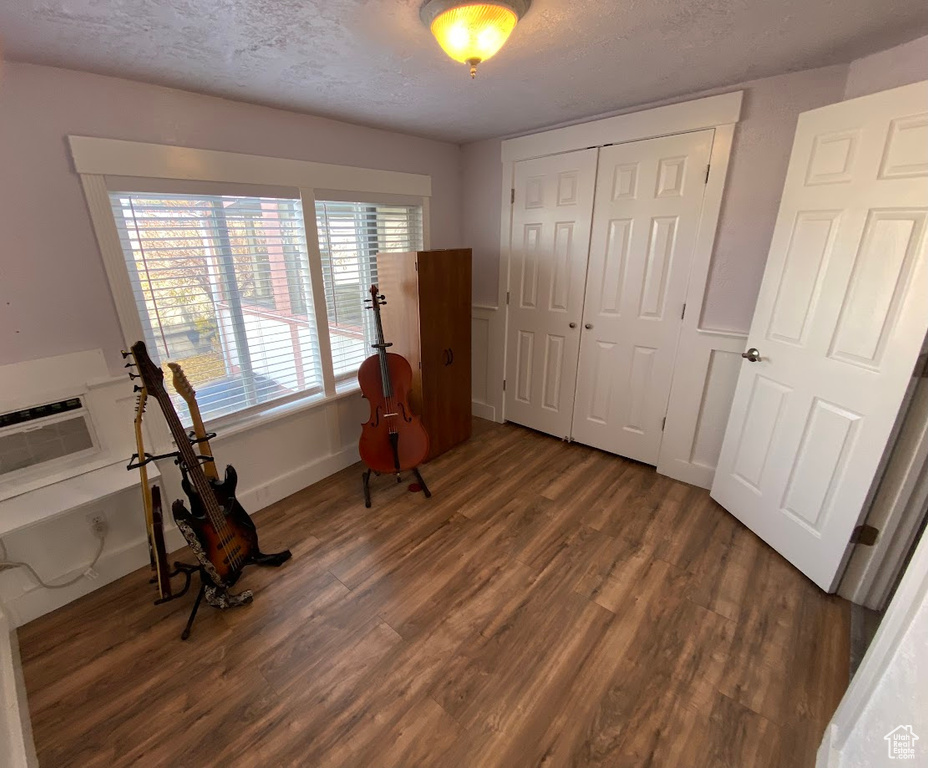 Living area with a textured ceiling, a wall mounted air conditioner, and dark wood-type flooring