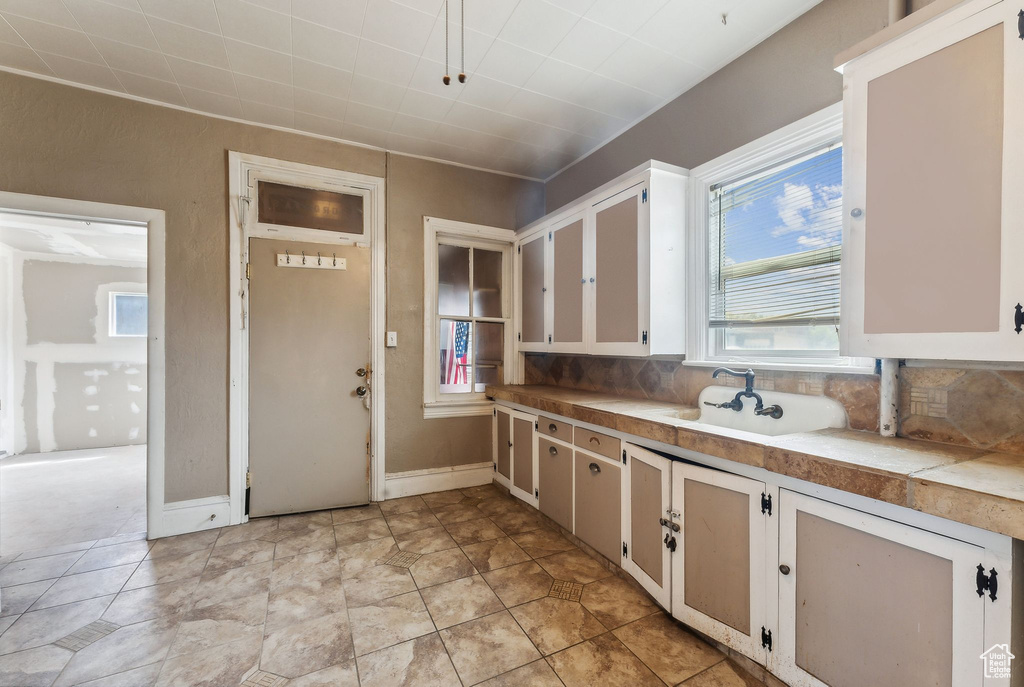 Kitchen with decorative backsplash, white cabinetry, sink, and light tile patterned floors