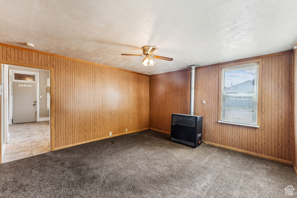 Spare room with a wood stove, wood walls, ceiling fan, and light colored carpet
