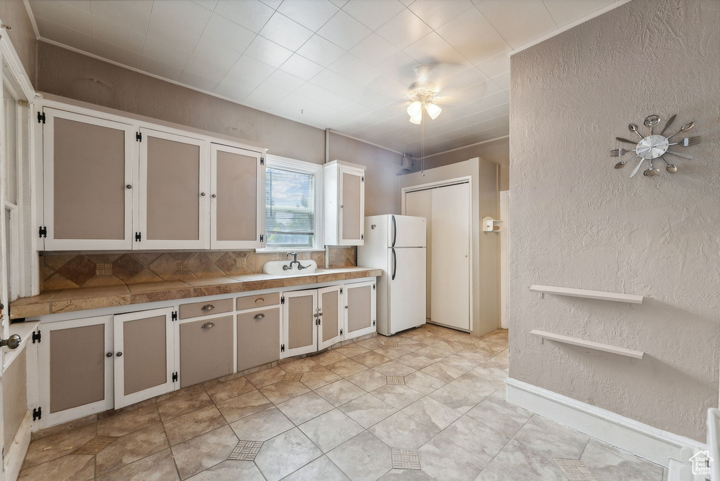 Kitchen with light tile patterned floors, white refrigerator, tasteful backsplash, and ceiling fan