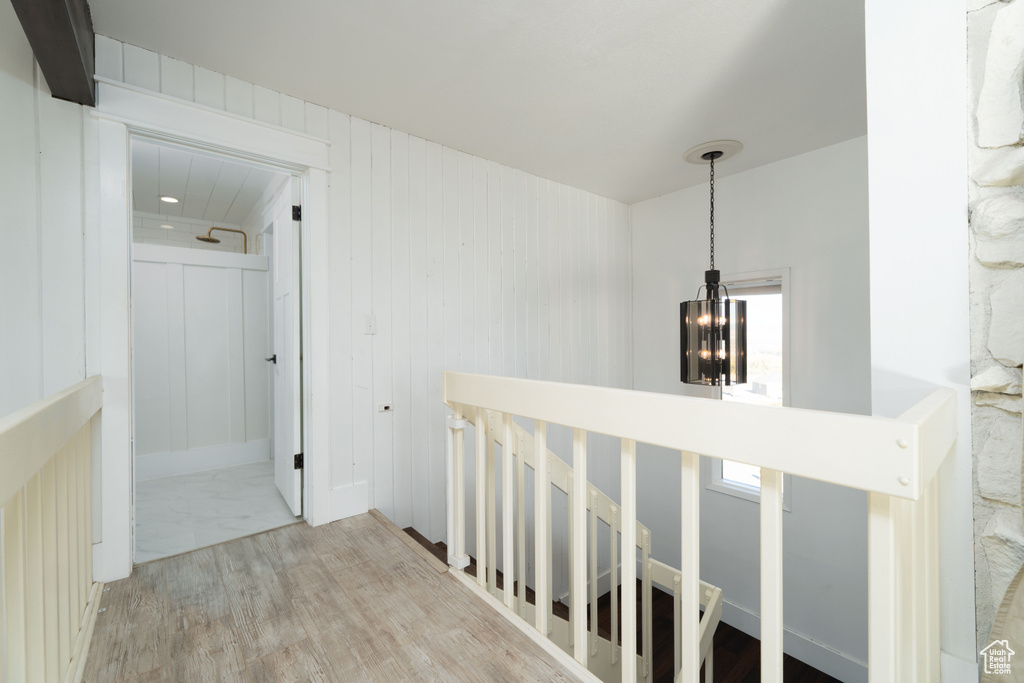 Hall featuring wooden walls, light hardwood / wood-style flooring, and an inviting chandelier