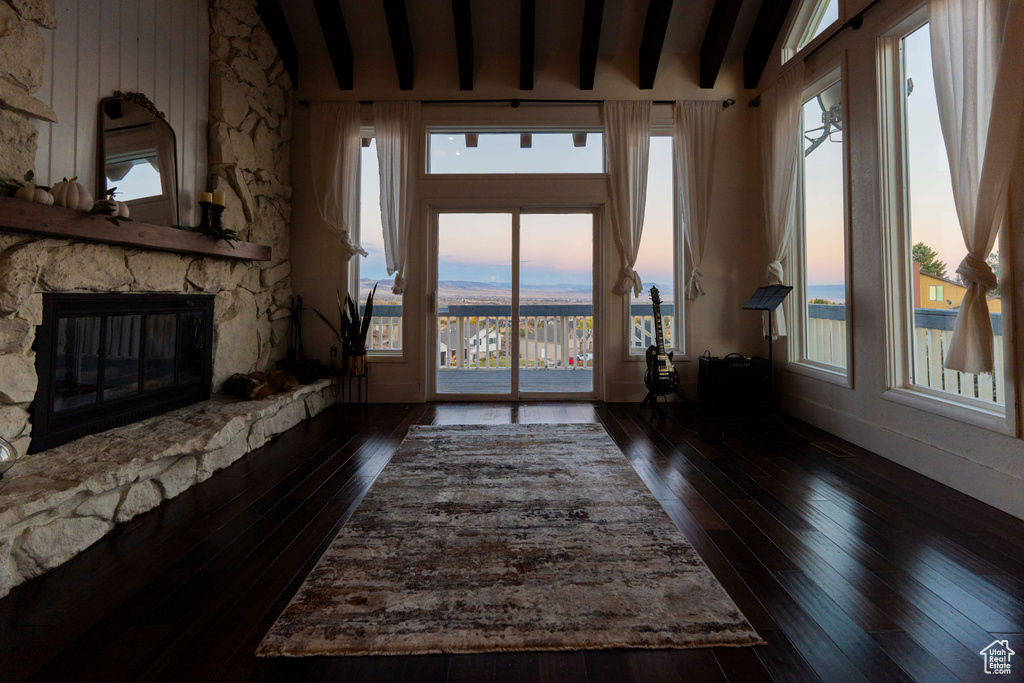 Living room with a wealth of natural light, a fireplace, lofted ceiling with beams, and dark hardwood / wood-style floors