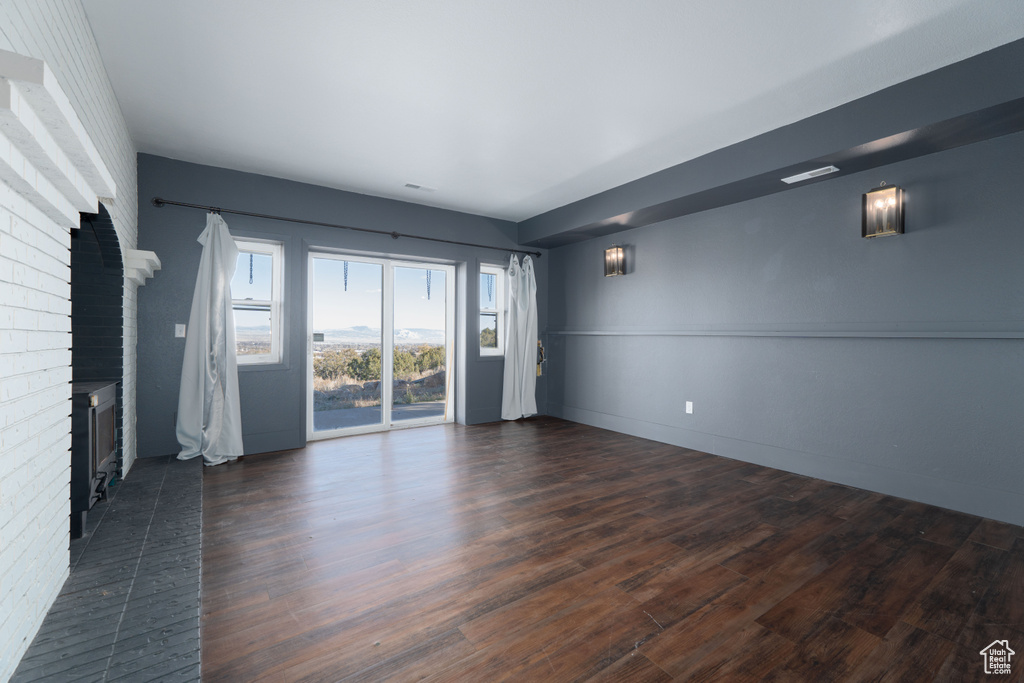 Empty room featuring dark hardwood / wood-style flooring and a brick fireplace