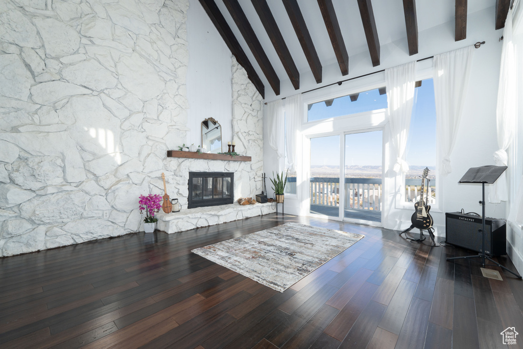 Living room with beam ceiling, dark wood-type flooring, high vaulted ceiling, and a stone fireplace