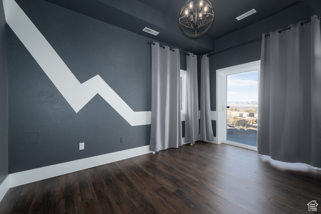 Spare room with dark hardwood / wood-style flooring and an inviting chandelier