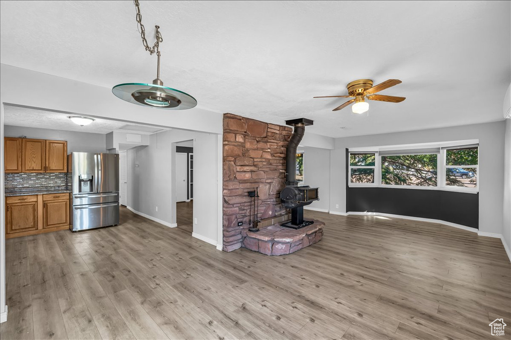 Unfurnished living room featuring light wood-type flooring, a wood stove, and ceiling fan