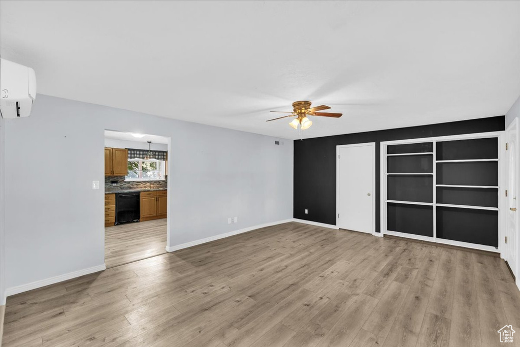 Unfurnished living room featuring ceiling fan, light wood-type flooring, and a wall mounted air conditioner