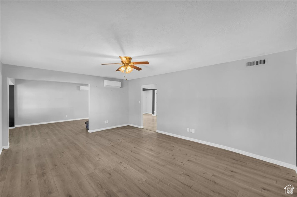 Empty room with ceiling fan, a wall mounted AC, and light hardwood / wood-style flooring