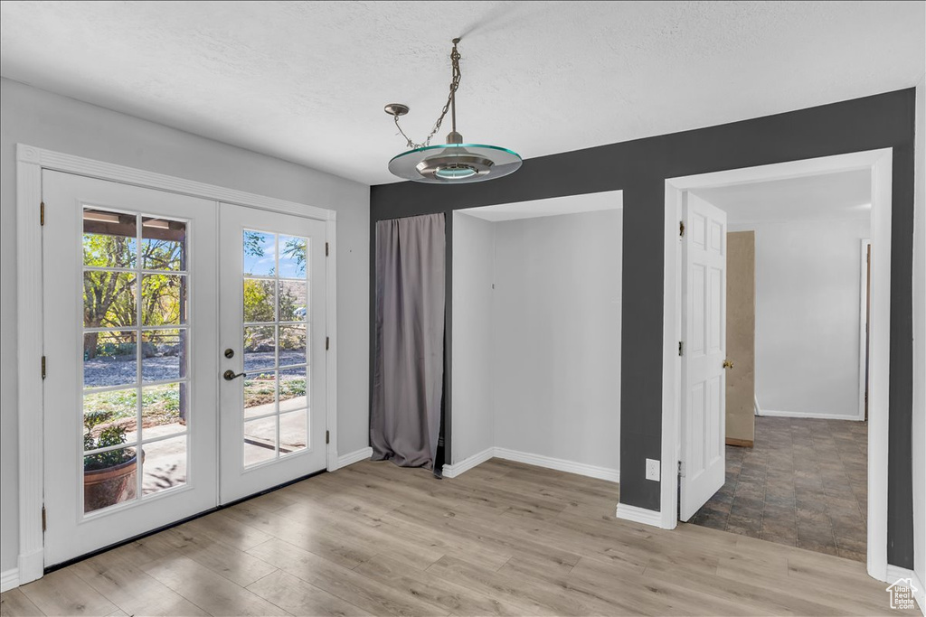 Unfurnished dining area featuring french doors, light hardwood / wood-style floors, and a textured ceiling