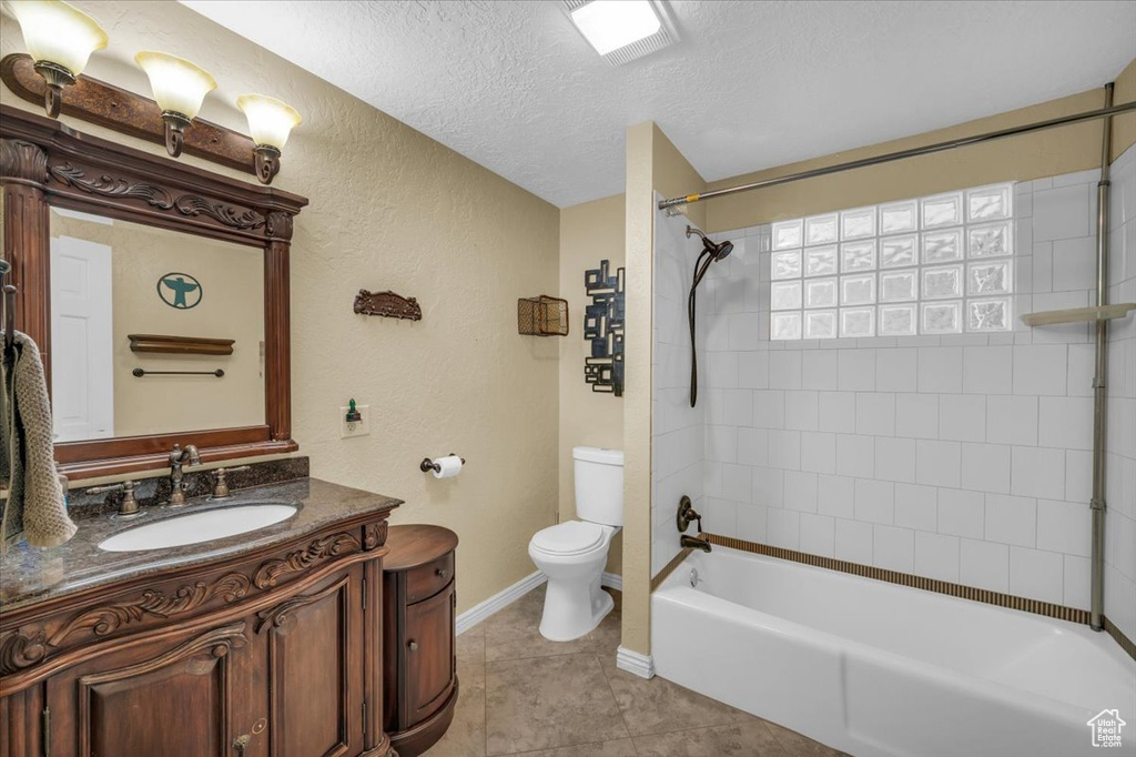 Full bathroom with toilet, tile patterned flooring, tiled shower / bath, a textured ceiling, and vanity