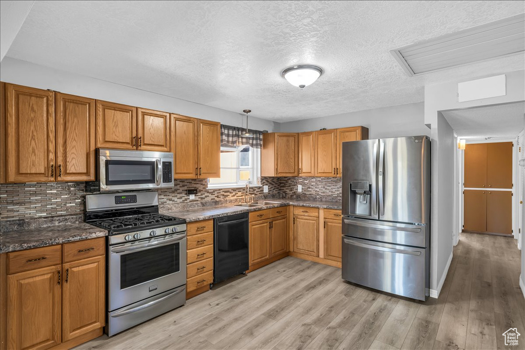 Kitchen with a textured ceiling, stainless steel appliances, light hardwood / wood-style floors, and dark stone countertops