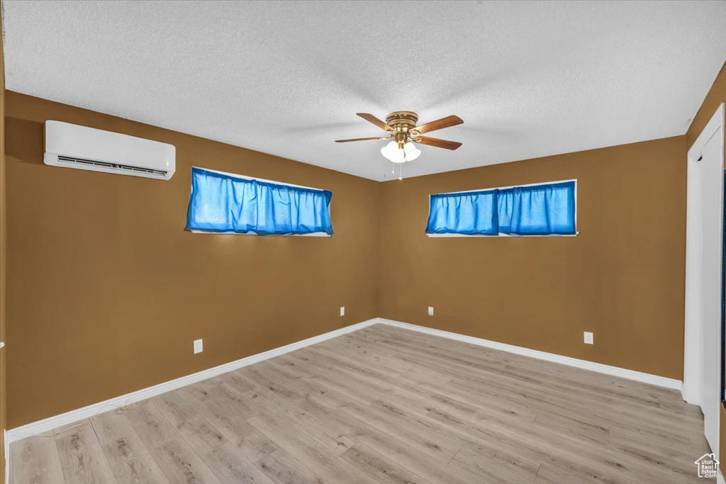 Unfurnished room featuring an AC wall unit, light wood-type flooring, a wealth of natural light, and a textured ceiling