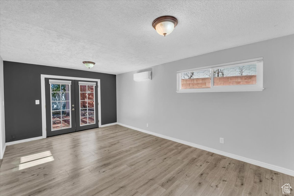 Spare room featuring a wall mounted AC, french doors, light hardwood / wood-style flooring, and a healthy amount of sunlight