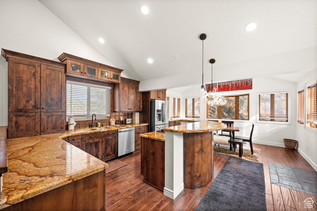 Kitchen with hanging light fixtures, dark hardwood / wood-style flooring, vaulted ceiling, a kitchen island, and appliances with stainless steel finishes