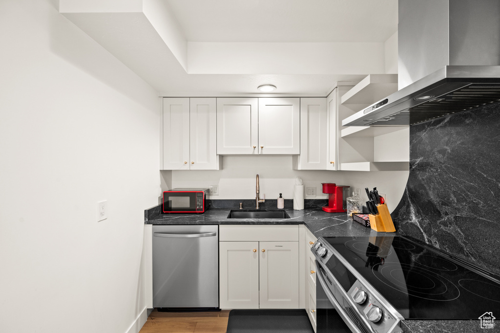 Kitchen featuring white cabinets, sink, wall chimney exhaust hood, and stainless steel appliances