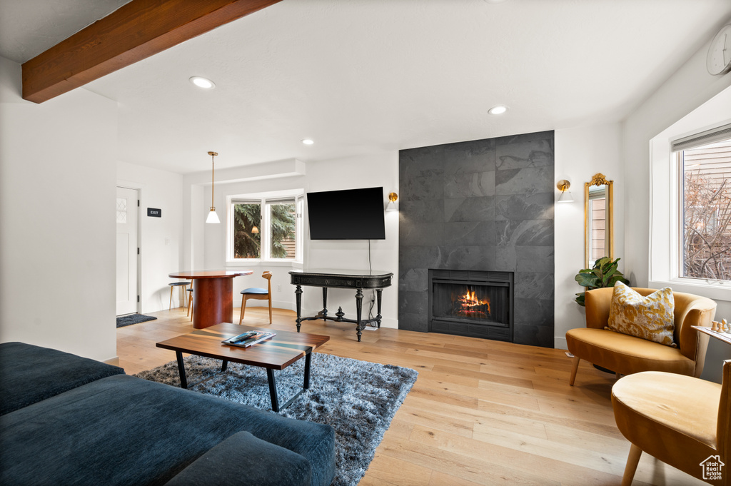 Living room featuring beamed ceiling, a tiled fireplace, and light hardwood / wood-style floors