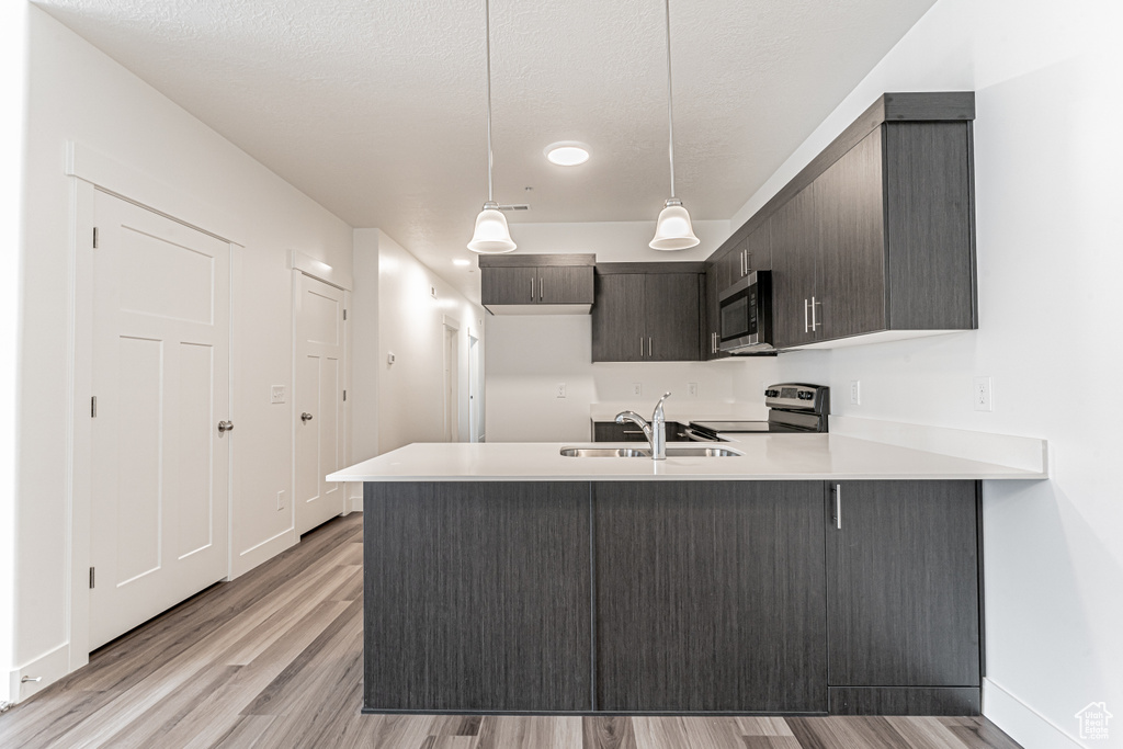 Kitchen with appliances with stainless steel finishes, a peninsula, light countertops, light wood-style floors, and a textured ceiling