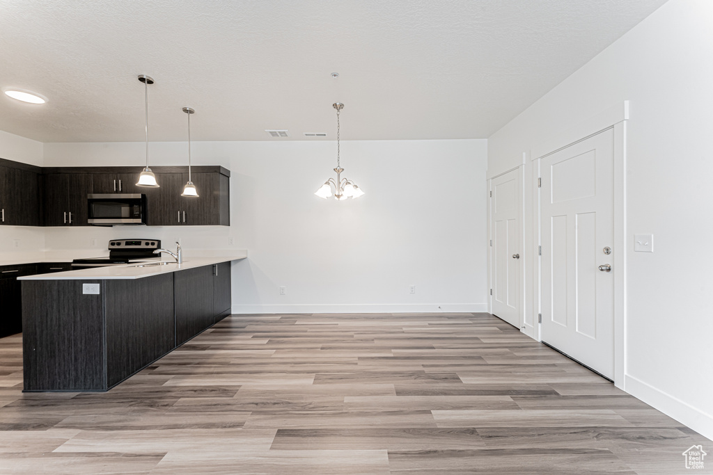 Kitchen featuring stainless steel appliances, a chandelier, light countertops, light wood finished floors, and baseboards