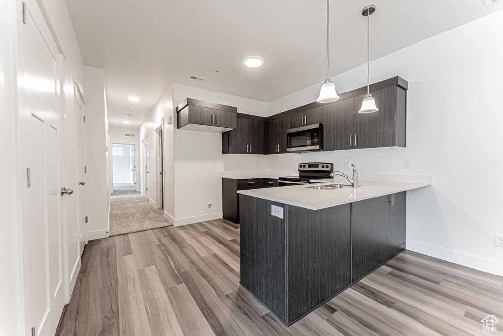 Kitchen featuring stainless steel appliances, a peninsula, light wood-style floors, and baseboards