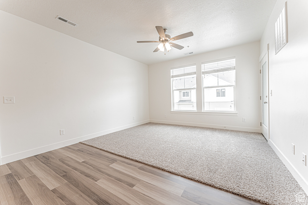 Unfurnished room with wood finished floors, a ceiling fan, baseboards, and a textured ceiling