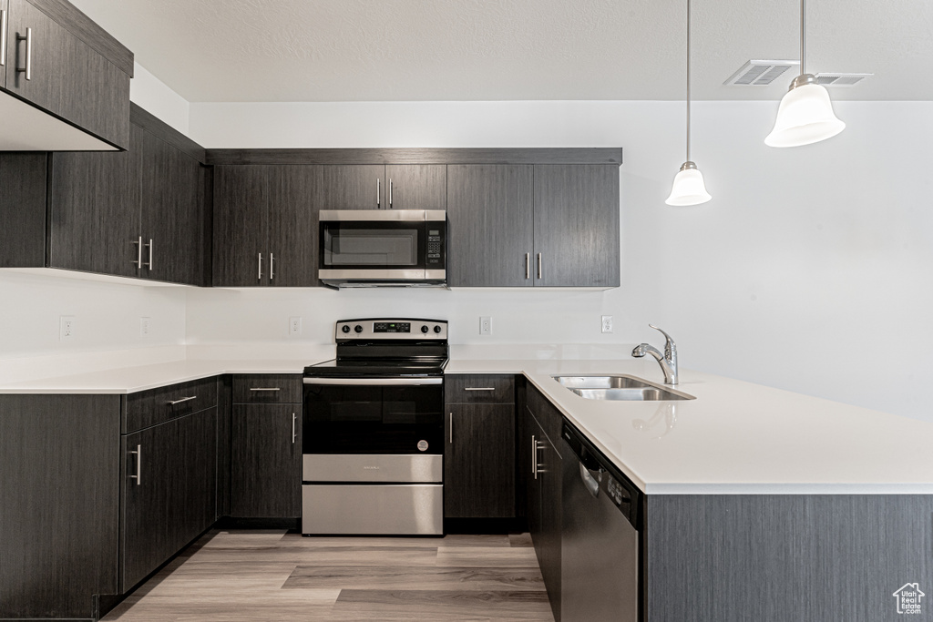 Kitchen with appliances with stainless steel finishes, a sink, a peninsula, light wood finished floors, and light countertops