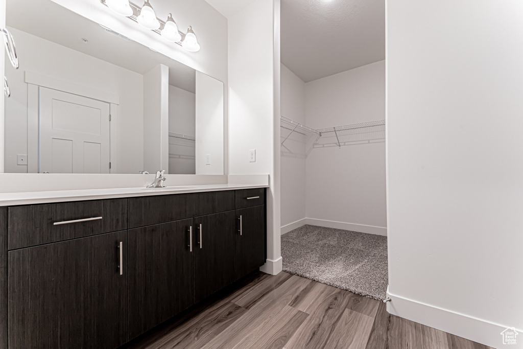 Bathroom featuring vanity, wood finished floors, baseboards, and a walk in closet
