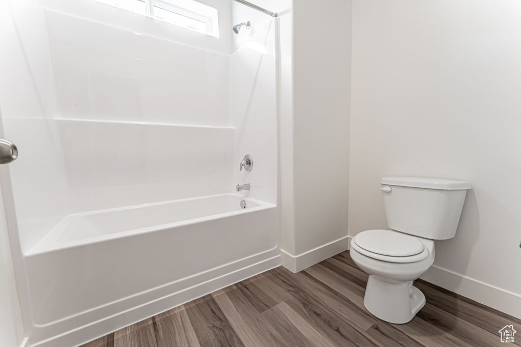 Bathroom featuring baseboards, toilet, shower / bath combination, and wood finished floors