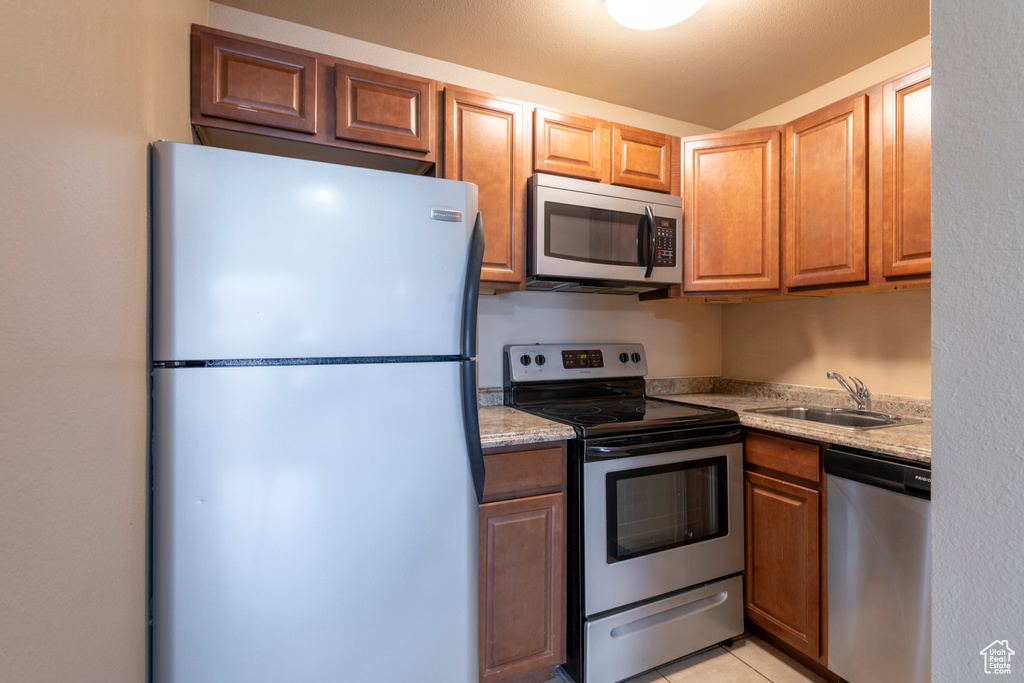 Kitchen featuring light stone countertops, sink, light tile patterned floors, and appliances with stainless steel finishes