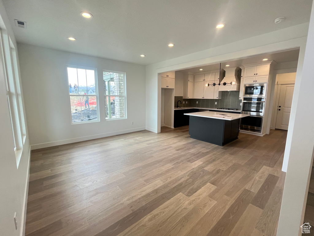 Kitchen with visible vents, premium range hood, white cabinetry, stainless steel appliances, and a kitchen island