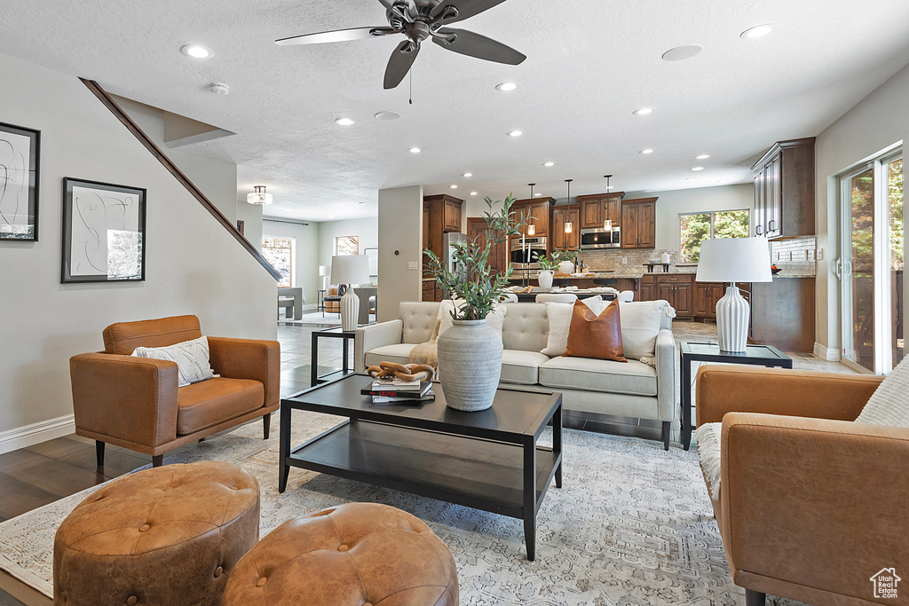 Living room with ceiling fan, light wood-type flooring, and a textured ceiling