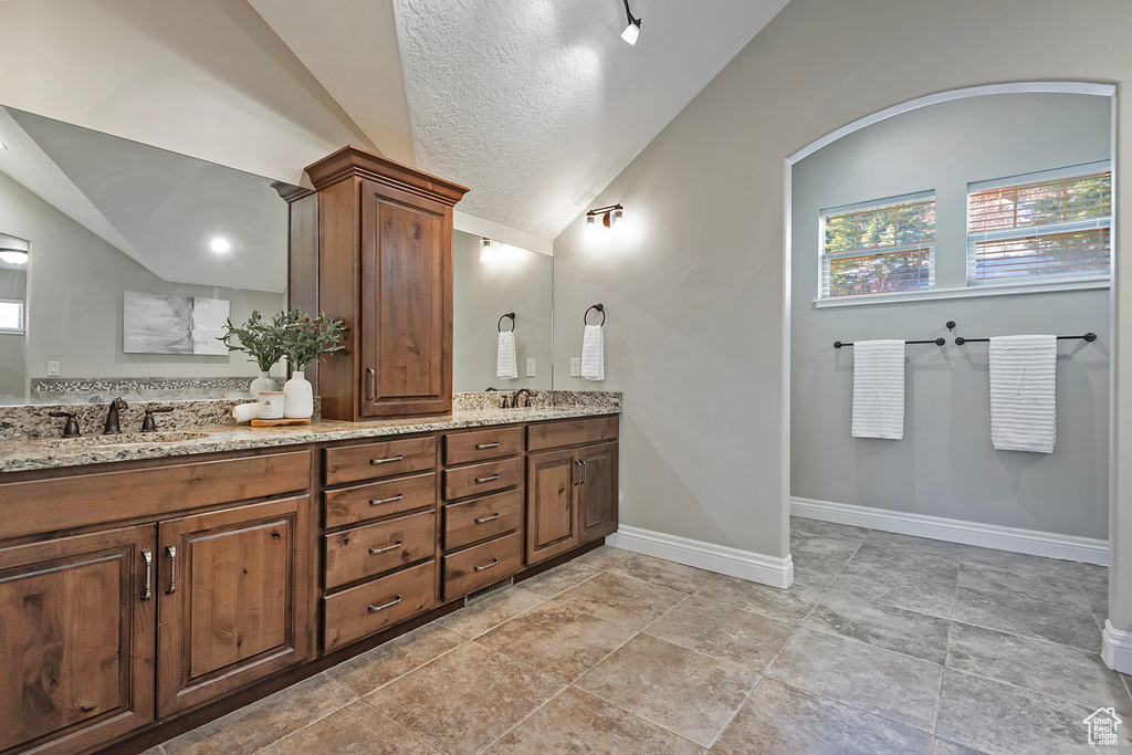 Bathroom with a textured ceiling, vanity, vaulted ceiling, and tile patterned floors