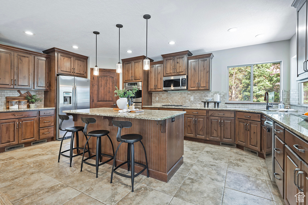 Kitchen featuring light stone countertops, appliances with stainless steel finishes, a center island, and sink