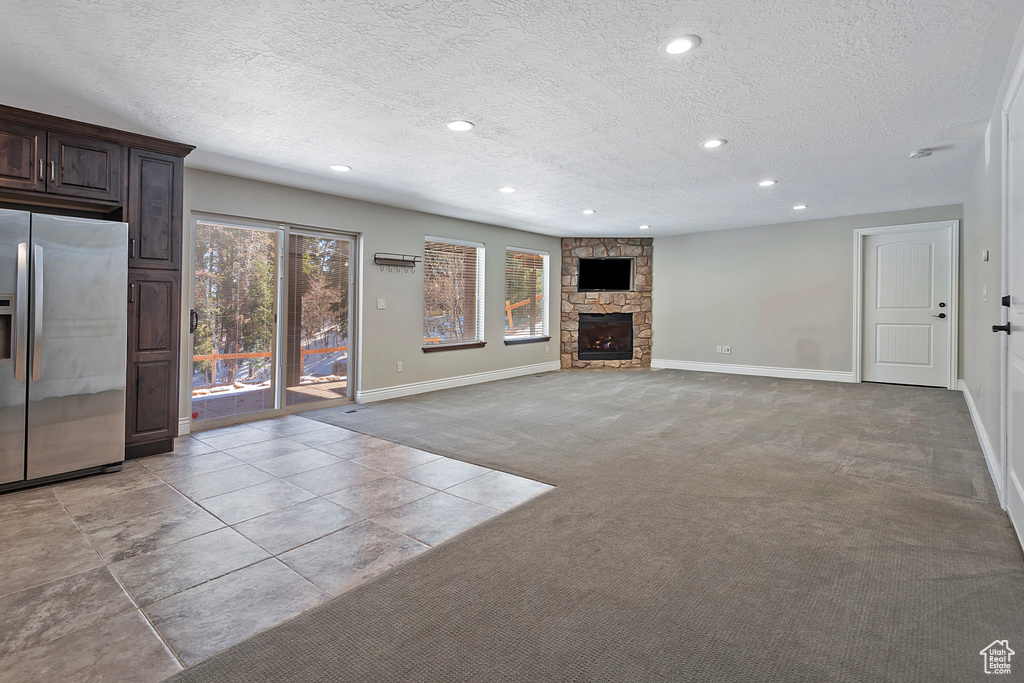 Unfurnished living room with a fireplace, light colored carpet, and a textured ceiling