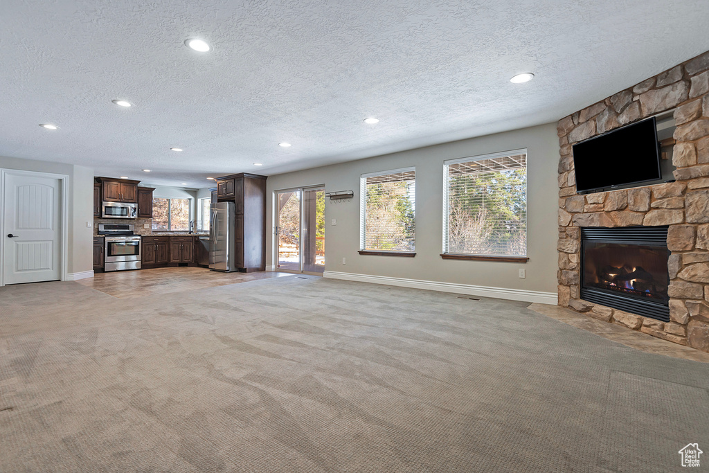 Unfurnished living room with a stone fireplace, a wealth of natural light, light colored carpet, and a textured ceiling