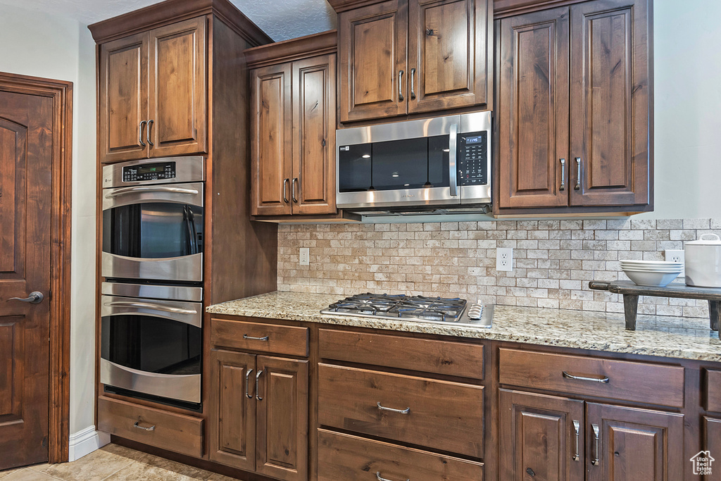 Kitchen featuring appliances with stainless steel finishes, tasteful backsplash, light stone counters, and dark brown cabinets