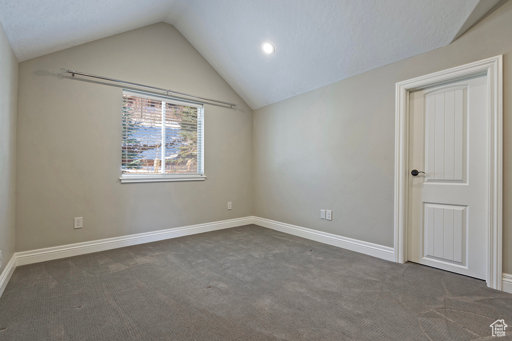 Empty room featuring dark carpet and vaulted ceiling