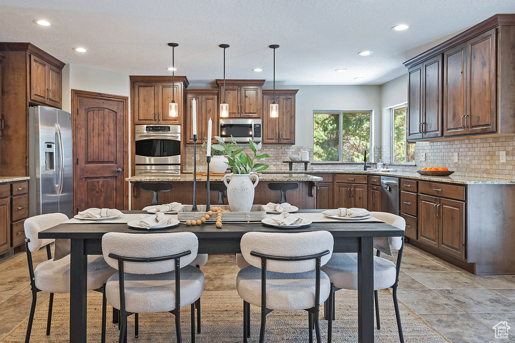 Kitchen featuring a center island, stainless steel appliances, light stone counters, pendant lighting, and decorative backsplash