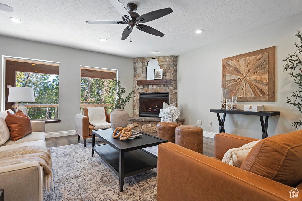 Living room featuring hardwood / wood-style floors, ceiling fan, a stone fireplace, and a textured ceiling