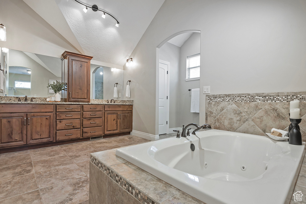 Bathroom featuring tile patterned flooring, vanity, a relaxing tiled tub, and vaulted ceiling