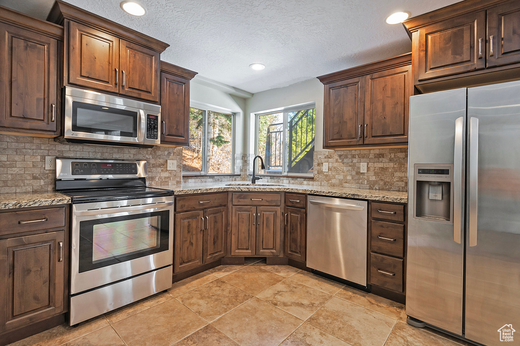 Kitchen featuring light stone countertops, sink, a textured ceiling, decorative backsplash, and appliances with stainless steel finishes