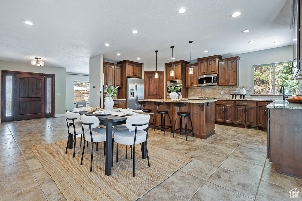 Kitchen with pendant lighting, a center island, light stone countertops, a kitchen bar, and stainless steel appliances