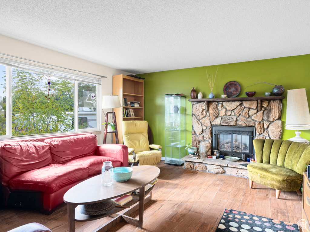 Living room featuring a stone fireplace, a textured ceiling, and hardwood / wood-style flooring