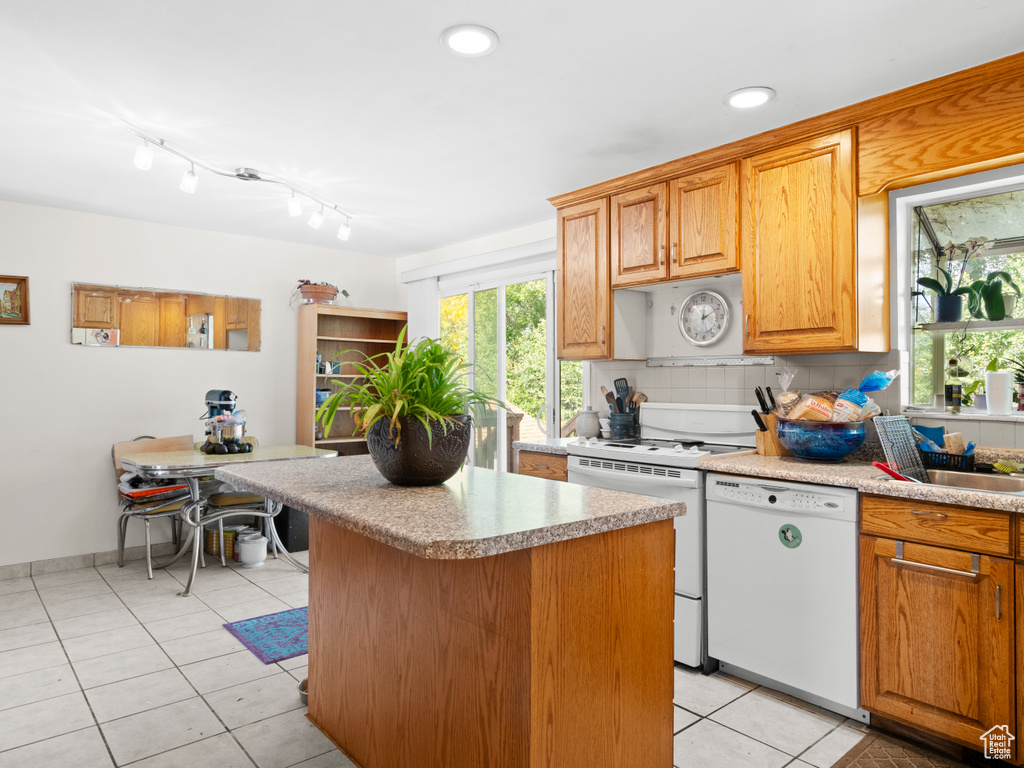 Kitchen featuring white appliances, light tile patterned floors, a kitchen island, and tasteful backsplash