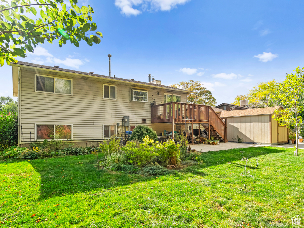 Back of property featuring a storage unit, a lawn, and a wooden deck